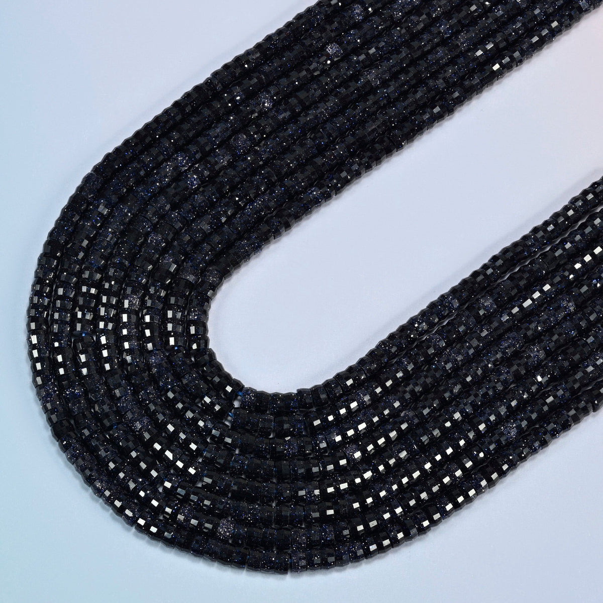Blue sandstone faceted heishi disc beads in several strands curved into a wide U, deep dark blue glass with fine glitter