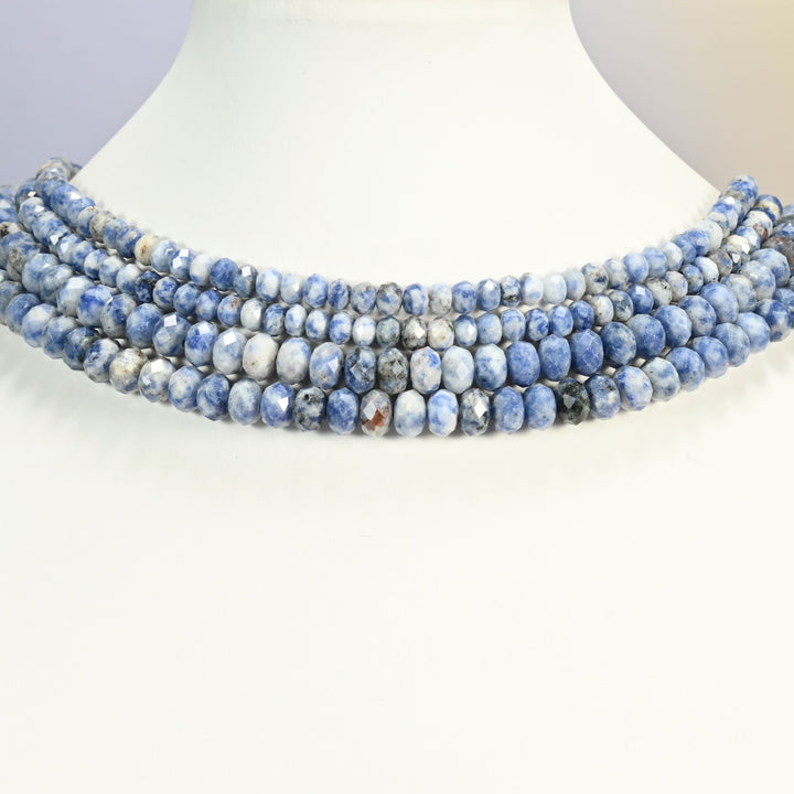 Blue spot jasper beads shown on a white neck display bust, the faceted rondelle strands sitting in even rows against the curve of the neck