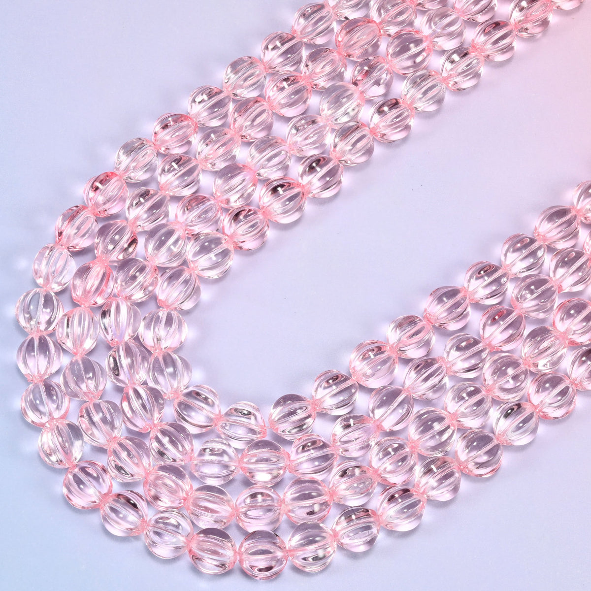Clear pink pumpkin glass beads, several strands laid in a wide sweeping curve across the frame.