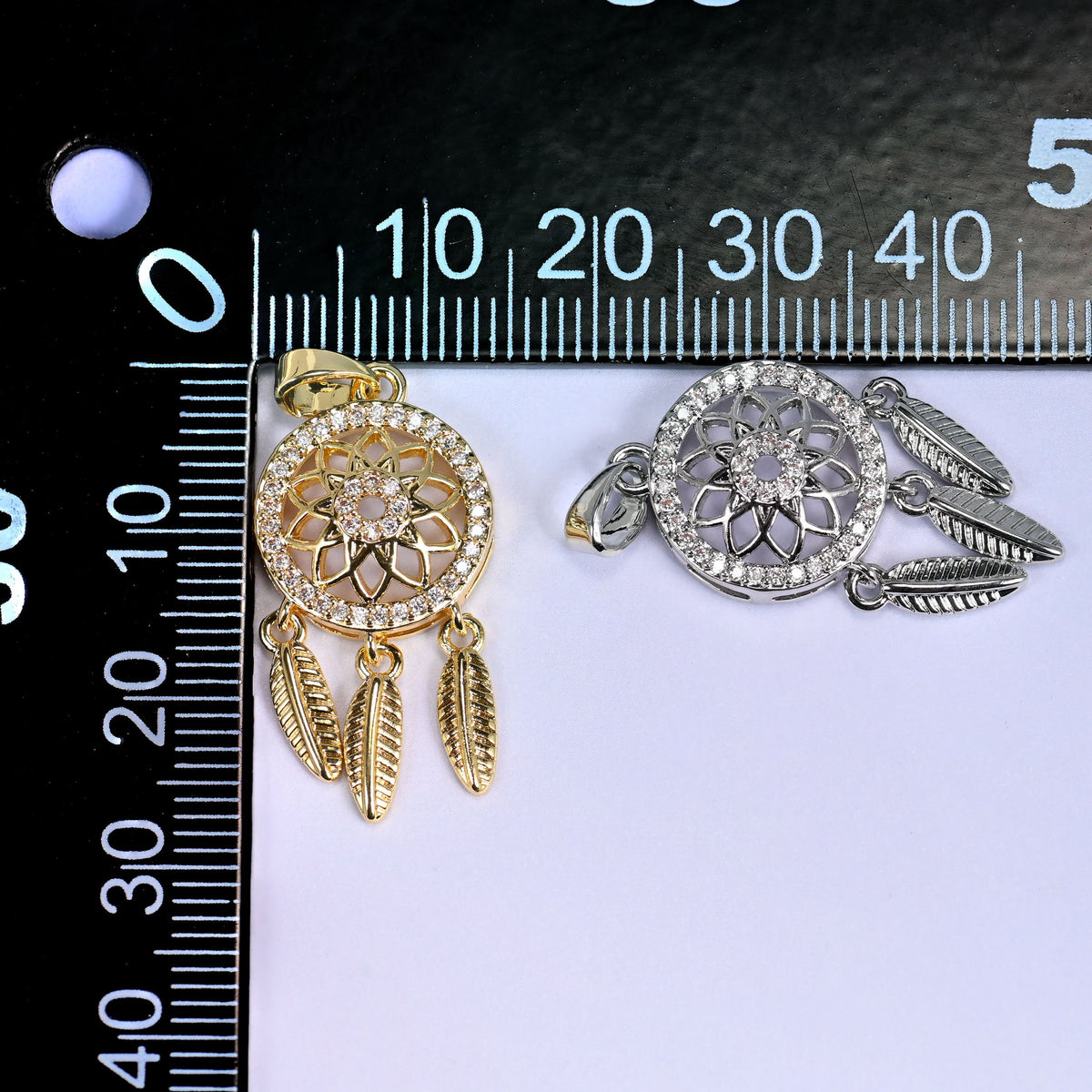 Gold and silver Dream Catcher Zirconia Charms laid on a black millimeter ruler, both finishes shown together against the mm markings.