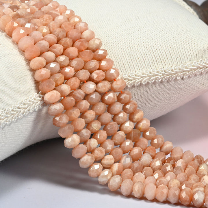 Peach moonstone faceted rondelle beads 5x8mm in warm peach orange with a pearly sheen, several strands draped over a white cushion