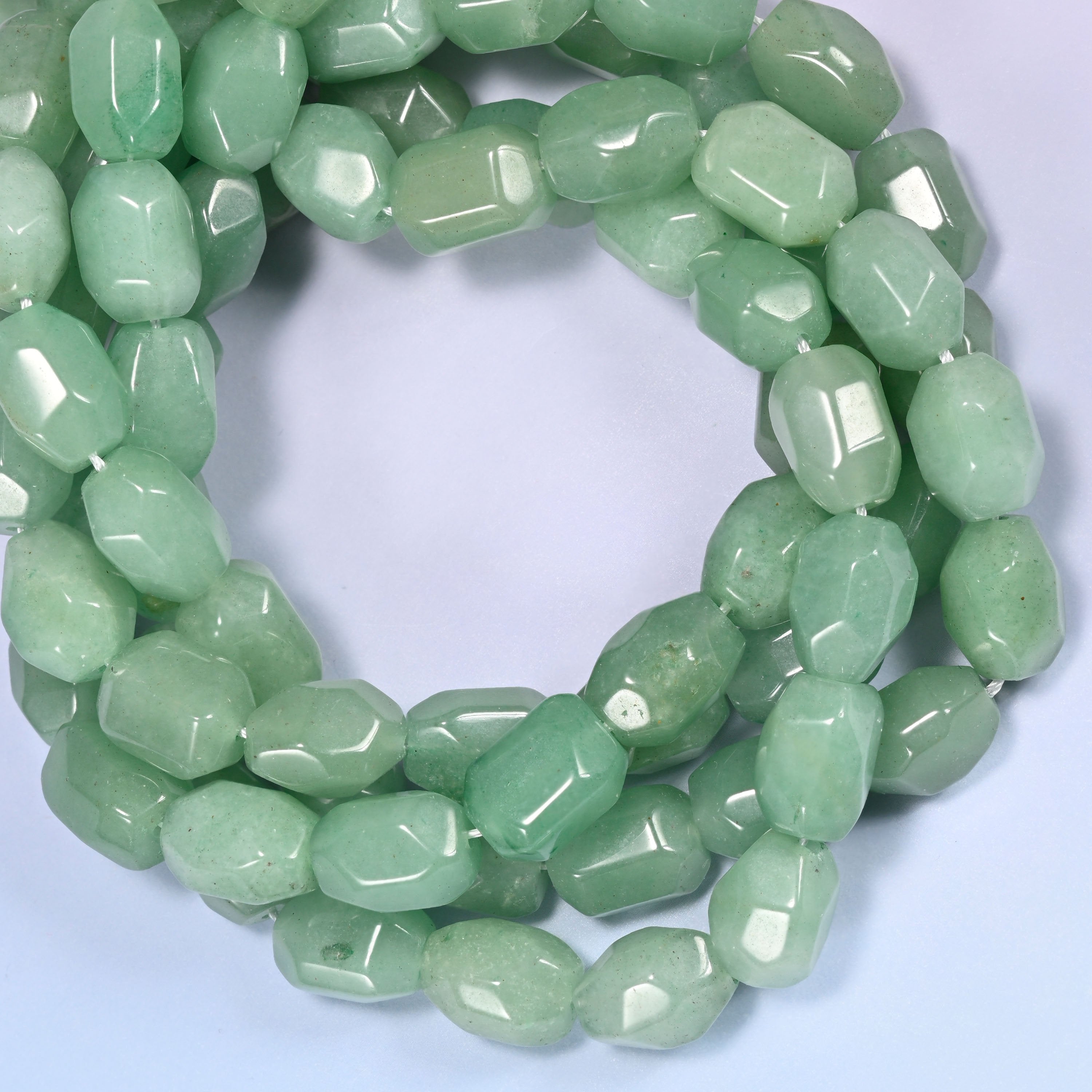 Wide circular coil of green faceted Aventurine barrel beads on a lavender and pink gradient background, showing the full wreath.