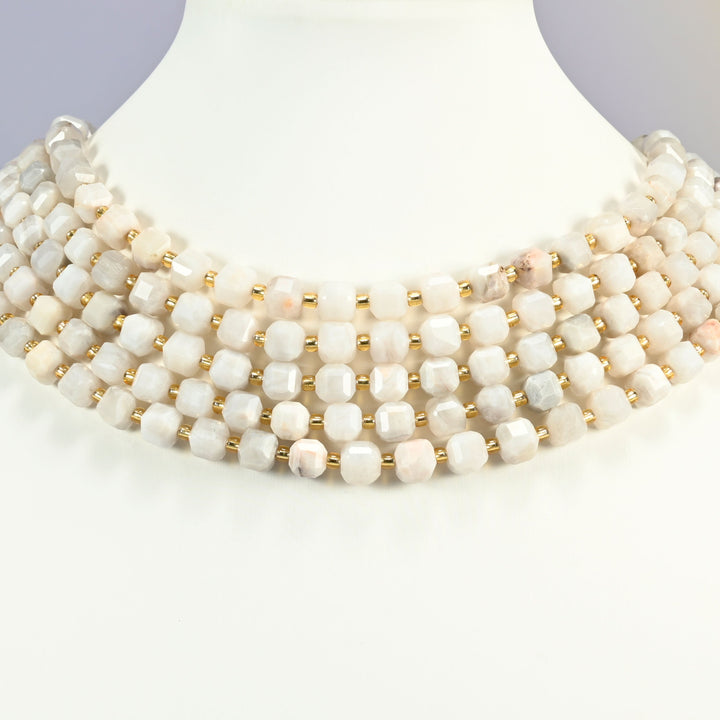 White crazy agate faceted cube strands arranged as a layered collar on a white display bust, cream white beads across the neck