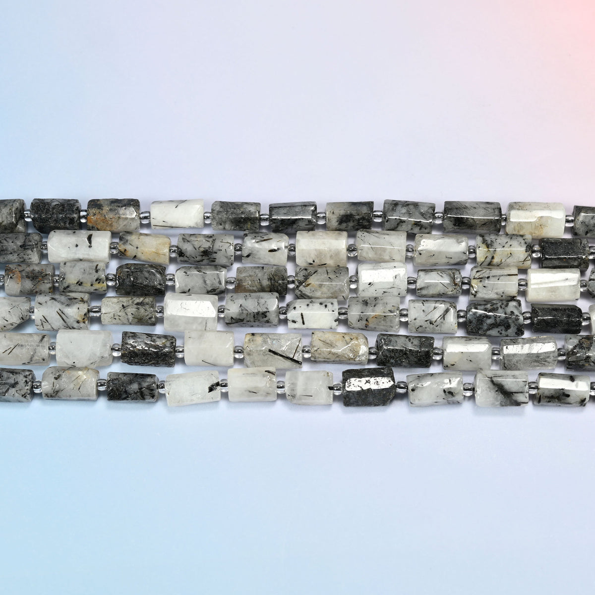 Several strands of black rutilated quartz faceted tube beads laid in straight rows with clear seed bead spacers