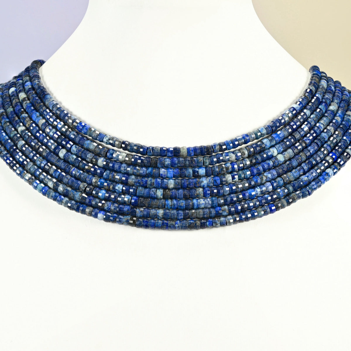 Dark blue lapis faceted heishi disc strands arranged as a layered collar on a white display bust, dark blue beads across the neck