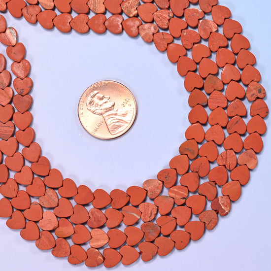 Matte red jasper flat heart beads in warm brick and terracotta red, finished matte so the surface reads as dry unglazed clay.