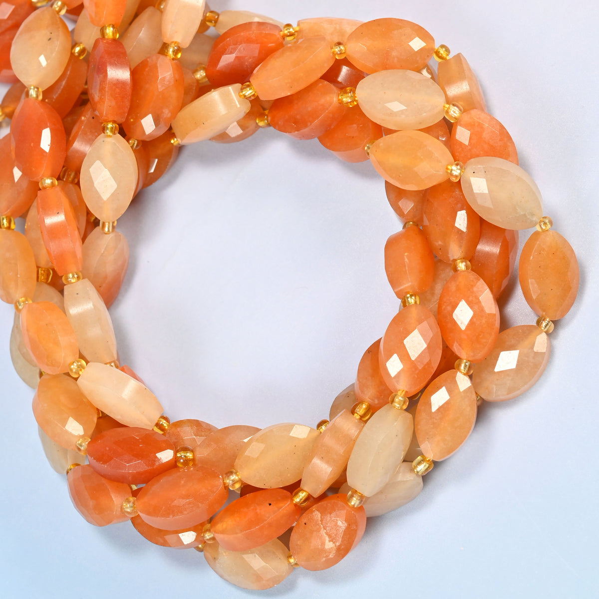 Red aventurine faceted flat oval beads coiled into overlapping loops, whole strands of warm orange stone
