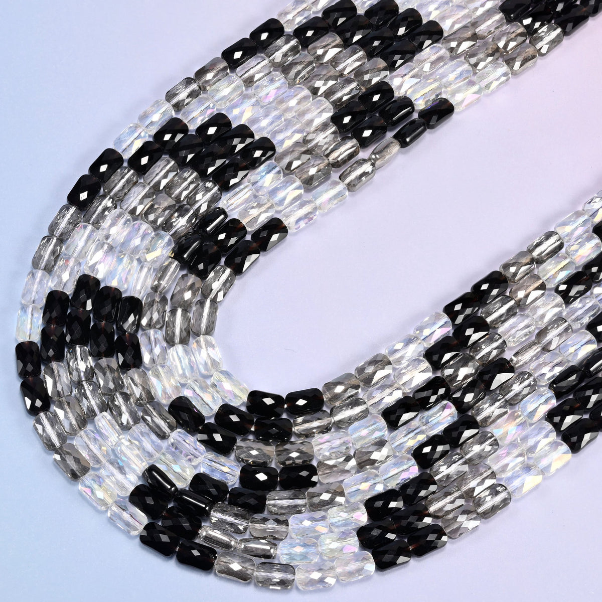 Black gray clear faceted rectangle glass beads hanging in a long U curve on a blue background.