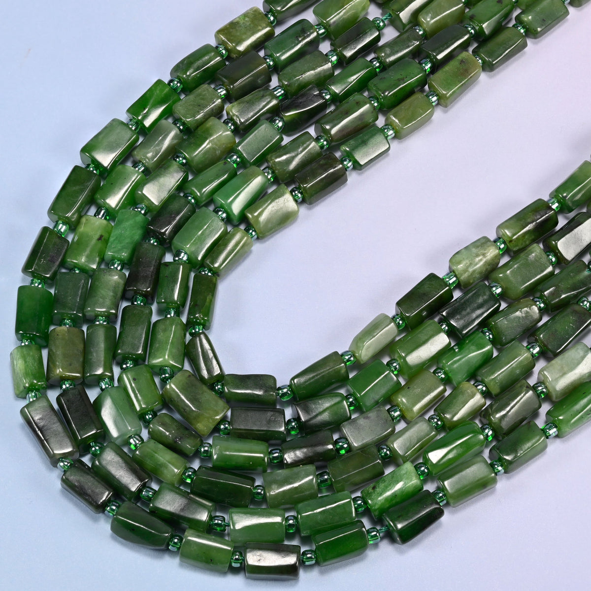 Canadian Green Jade faceted tube beads curving in a wide U across the frame, deep forest green shading into lighter sage green
