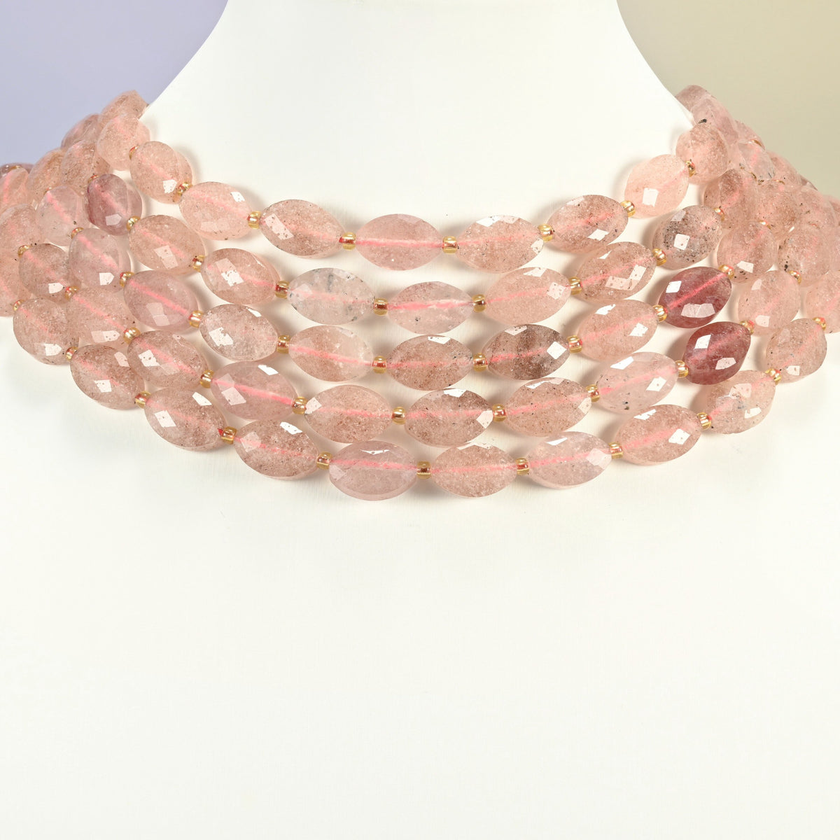 Strawberry quartz faceted flat oval strands arranged as a layered collar on a white display bust, soft pink beads across the neck