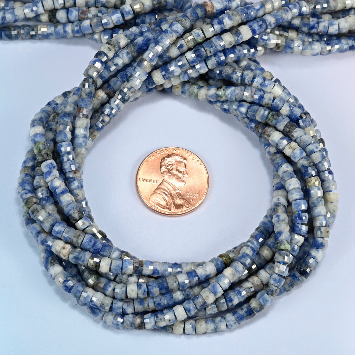 Blue spot jasper faceted heishi disc beads 2x4mm coiled in a loop around a US penny for scale, close-up of the faceted disc shape