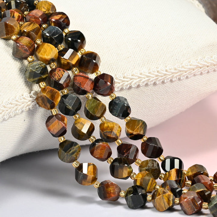 Tricolor tiger eye faceted spiral twist beads 10mm with small gold spacer beads, several strands draped over a white cushion
