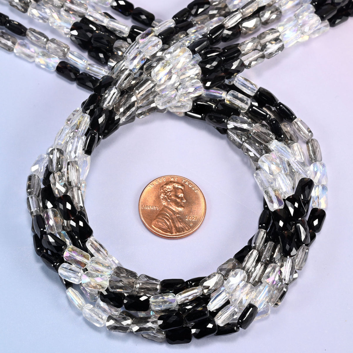 Black gray clear faceted rectangle glass beads circling a US penny laid flat inside the loop.