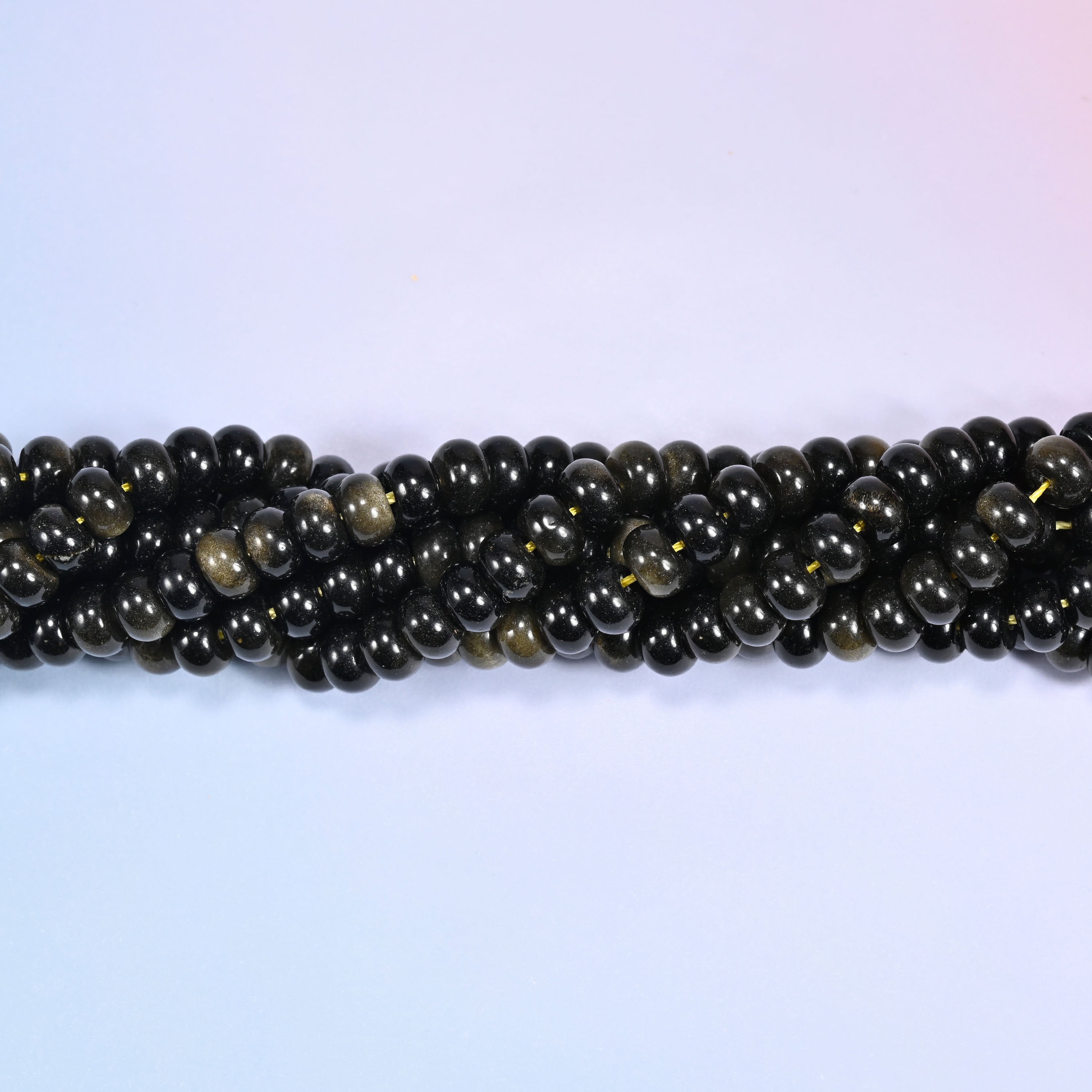 Close-up of coiled Gold Obsidian beads showing the glossy black surface and golden shimmer.