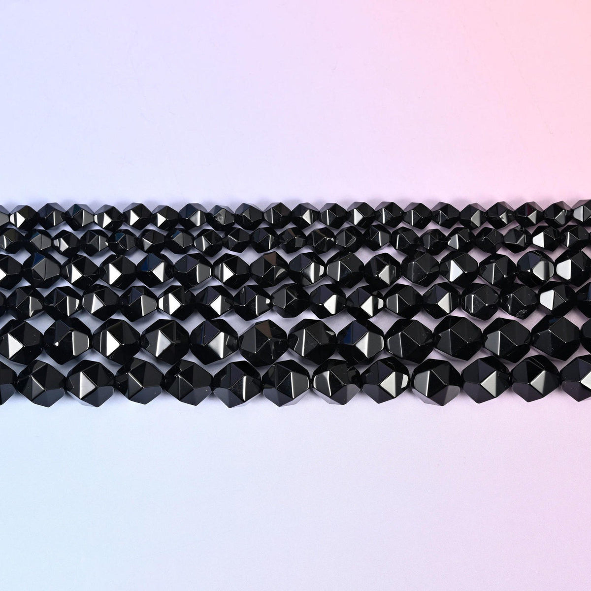 Black Onyx faceted beads in flat horizontal rows against a soft pink background, sold per 15.5 inch strand