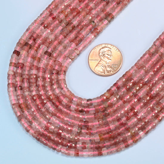 Close view of strawberry quartz faceted heishi disc strands curving beside a US penny for scale