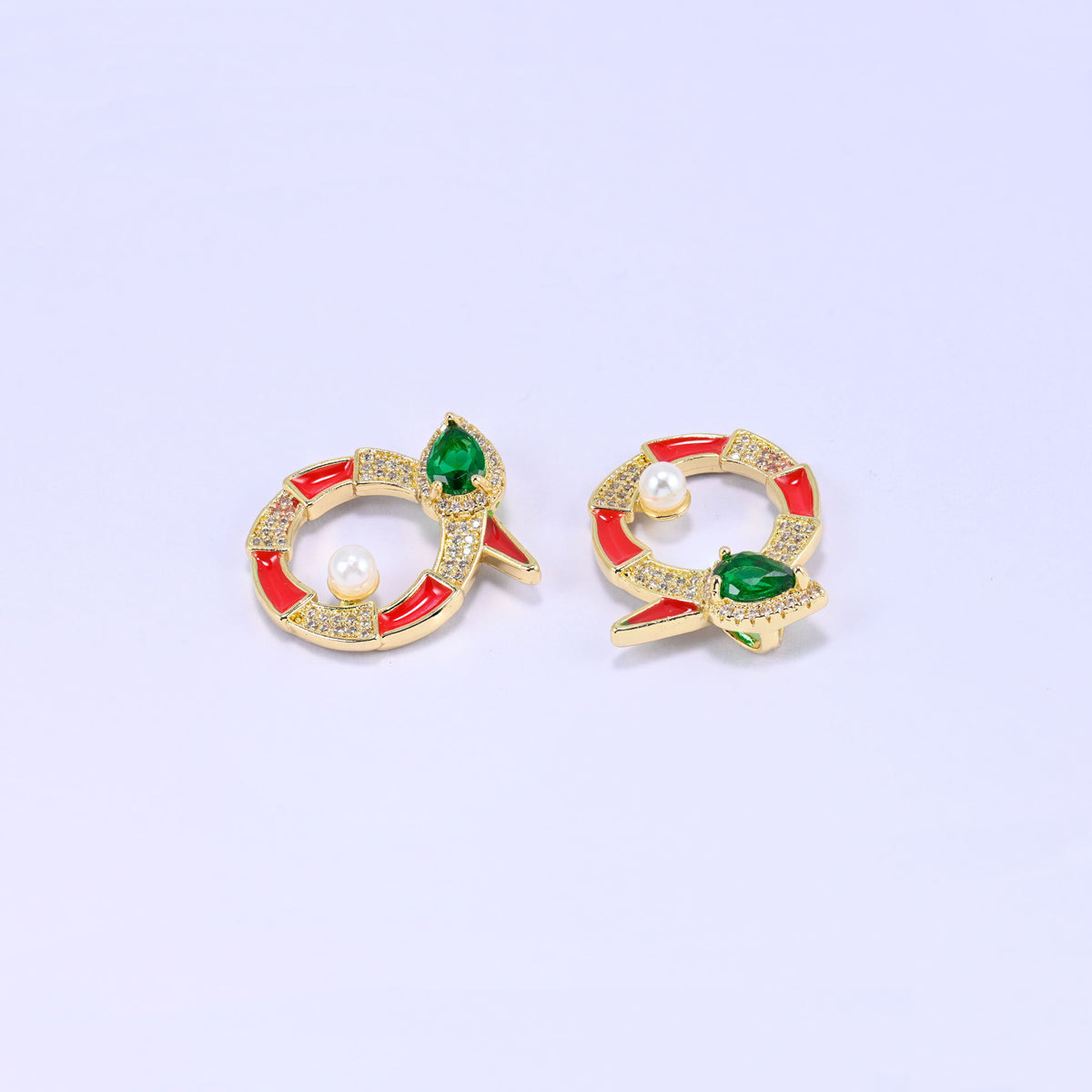 Two red round snake charms tilted on lavender, both showing the pear cut green stone head, tapered tail and pave zircon around the open ring.