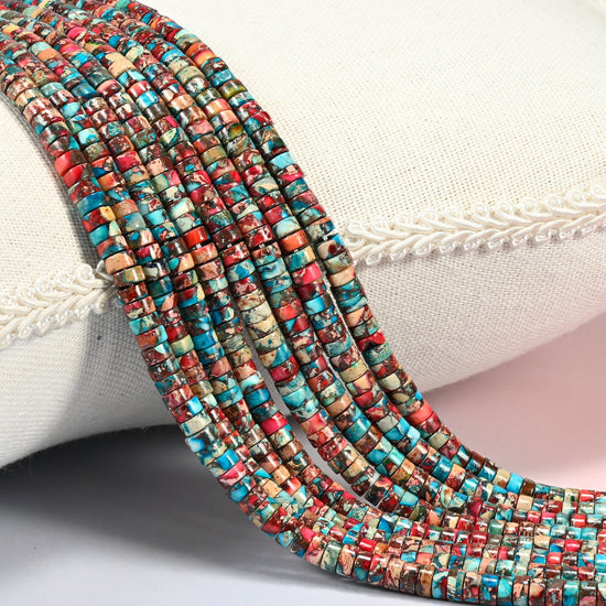 Dyed red blue sea sediment jasper heishi disc beads 2x4mm, several strands of turquoise, brick red and cream discs draped over a white cushion