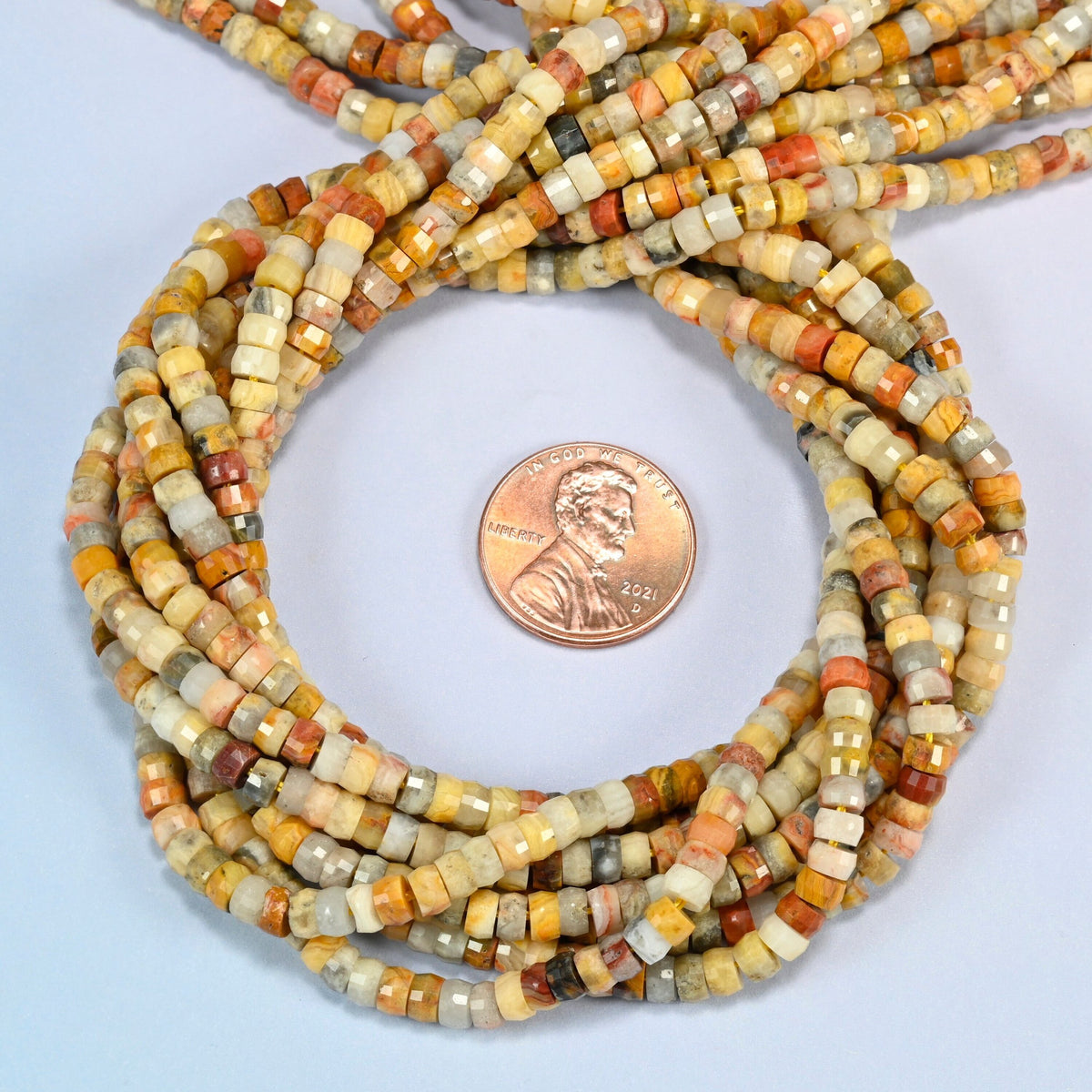 Crazy agate faceted heishi disc beads 2x4mm coiled in a loop around a US penny for scale, close-up of the faceted disc shape