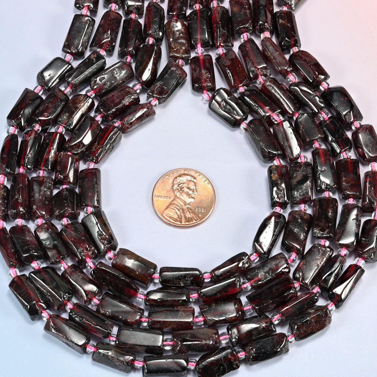 Red garnet tube strands formed into a teardrop loop around a US penny for scale