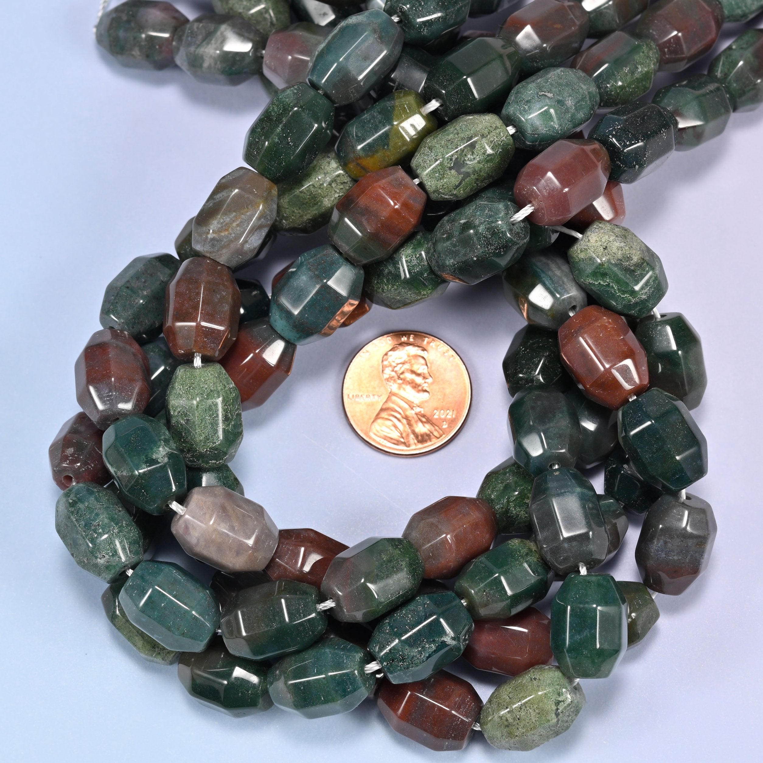 Close-up horizontal row of Indian Agate faceted barrel beads laid straight, showing the polished facet detail up close.