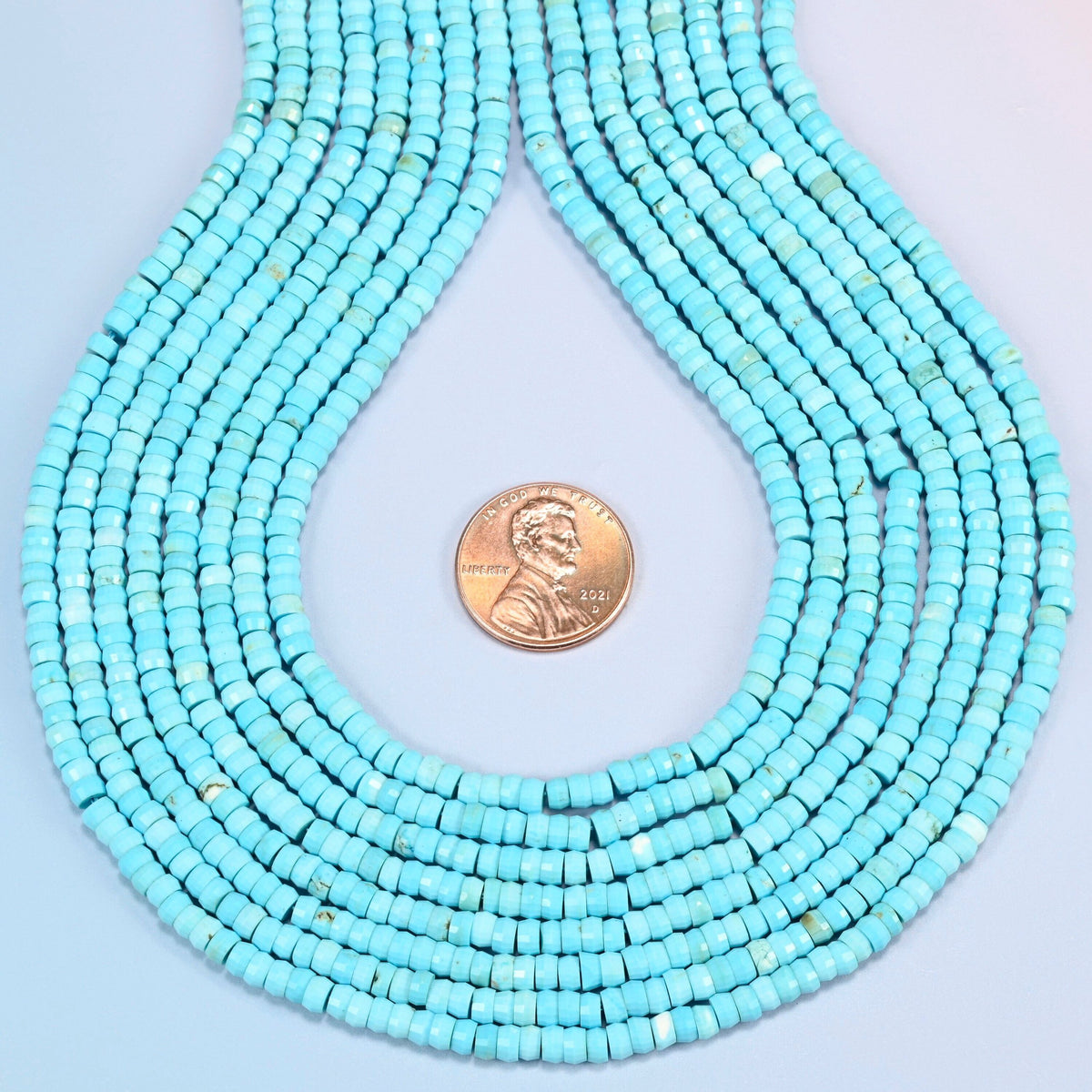 Dyed blue howlite faceted heishi disc strands formed into a teardrop loop around a US penny for scale