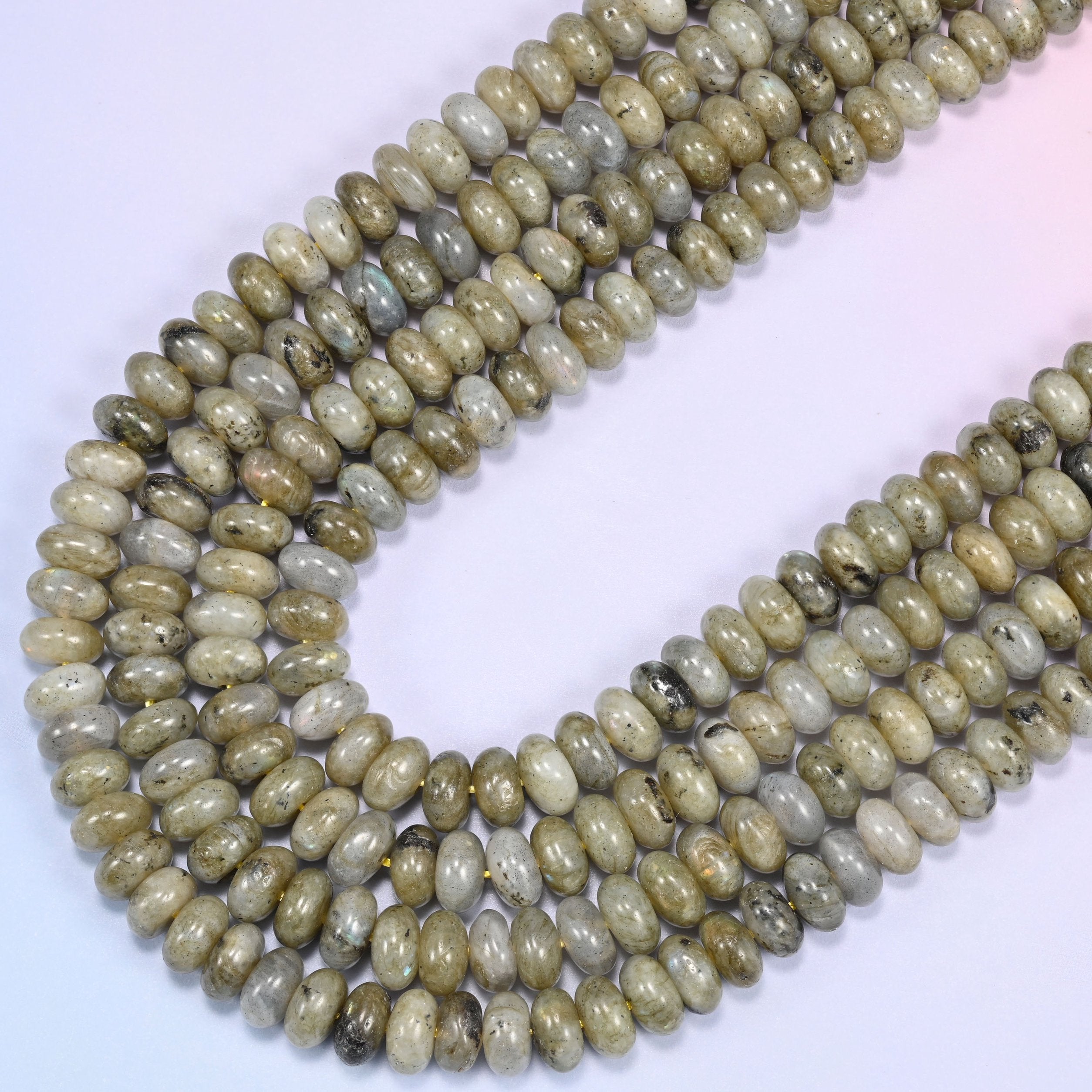 Close-up of Grey Labradorite rondelle beads coiled in a circular arrangement on a lavender background.