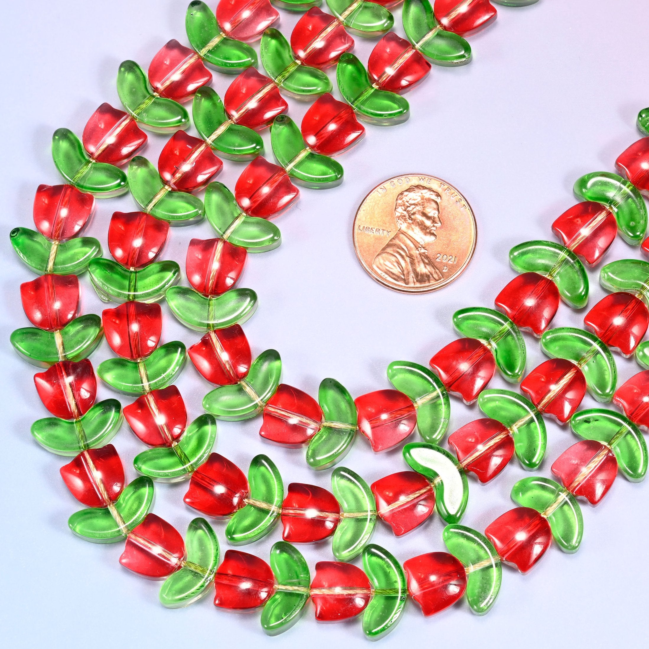 Wide view of a circular coil of red tulip and green leaf glass bead strands on a lavender and pink gradient background.