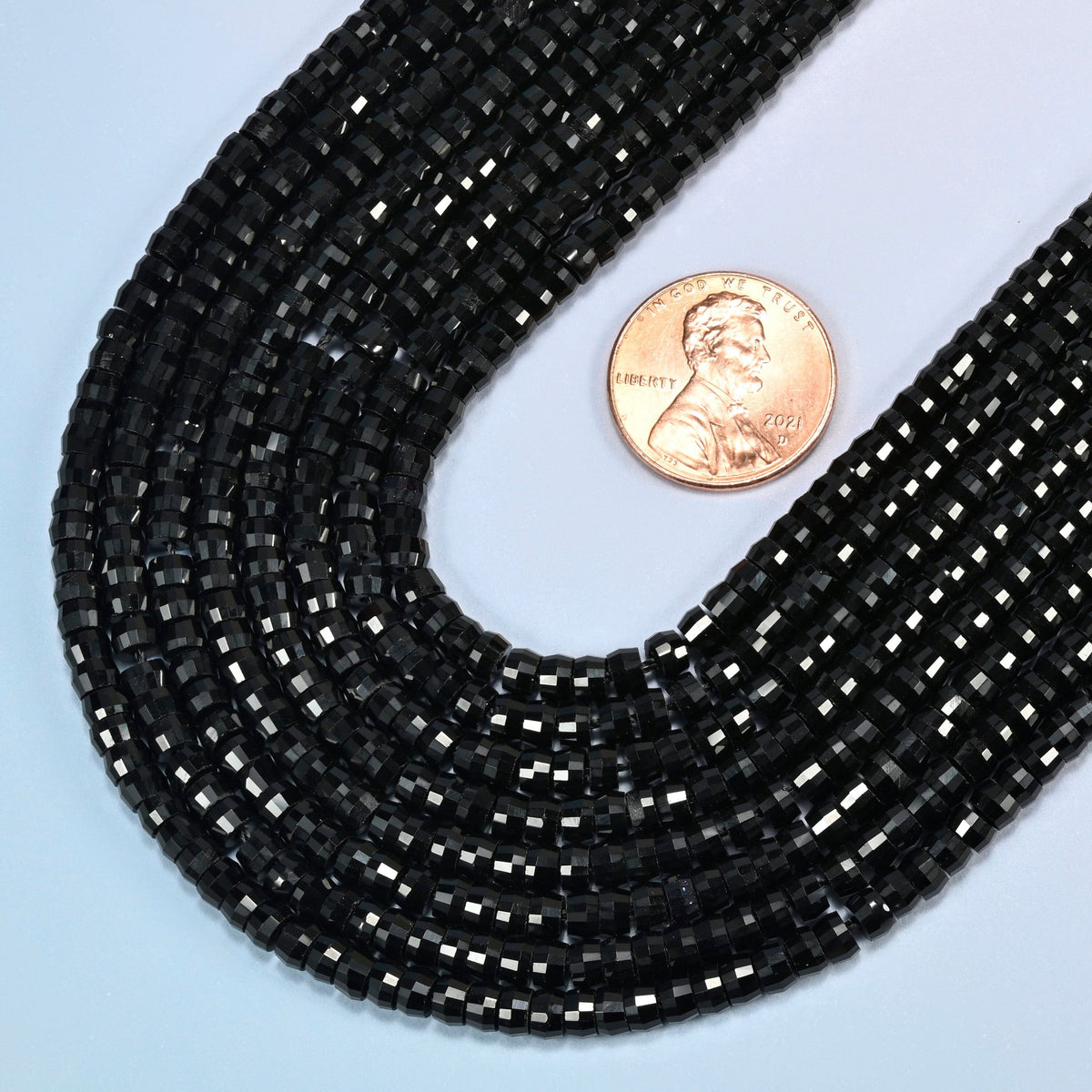 Close view of black onyx faceted heishi disc strands curving beside a US penny for scale