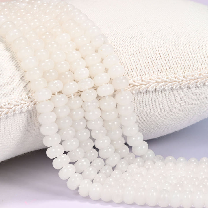 Close-up of multiple strands of polished White Jade rondelle beads with a soft milky glow, draped over a cream fabric jewelry display bust.