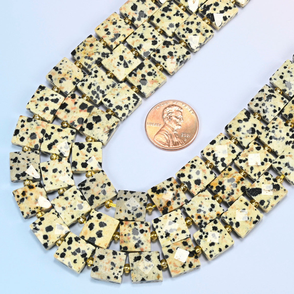 Close view of dalmatian jasper faceted flat square strands curving beside a US penny for scale