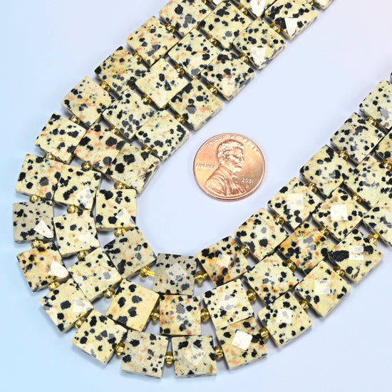 Close view of dalmatian jasper faceted flat square strands curving beside a US penny for scale