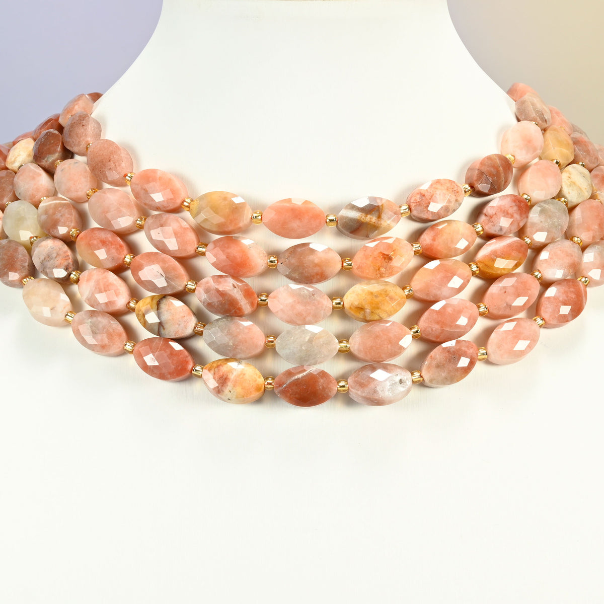 Red crazy agate faceted flat oval strands arranged as a layered collar on a white display bust, peach and copper beads across the neck