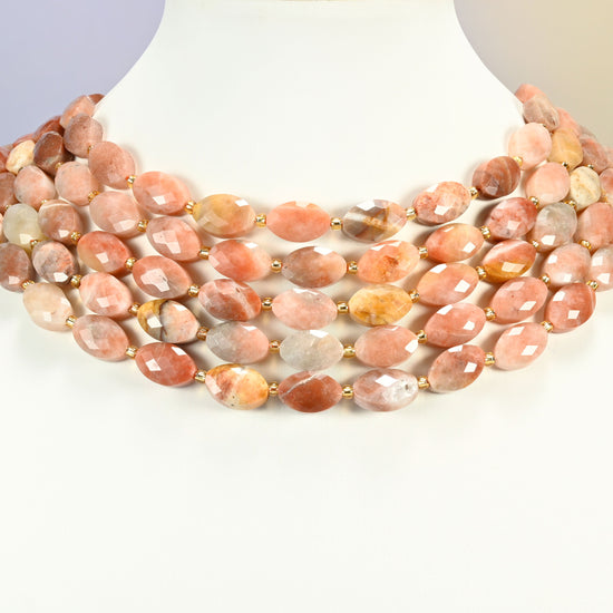 Red crazy agate faceted flat oval strands arranged as a layered collar on a white display bust, peach and copper beads across the neck