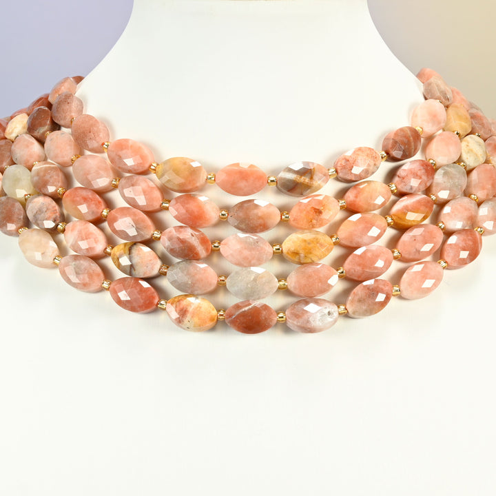 Red crazy agate faceted flat oval strands arranged as a layered collar on a white display bust, peach and copper beads across the neck
