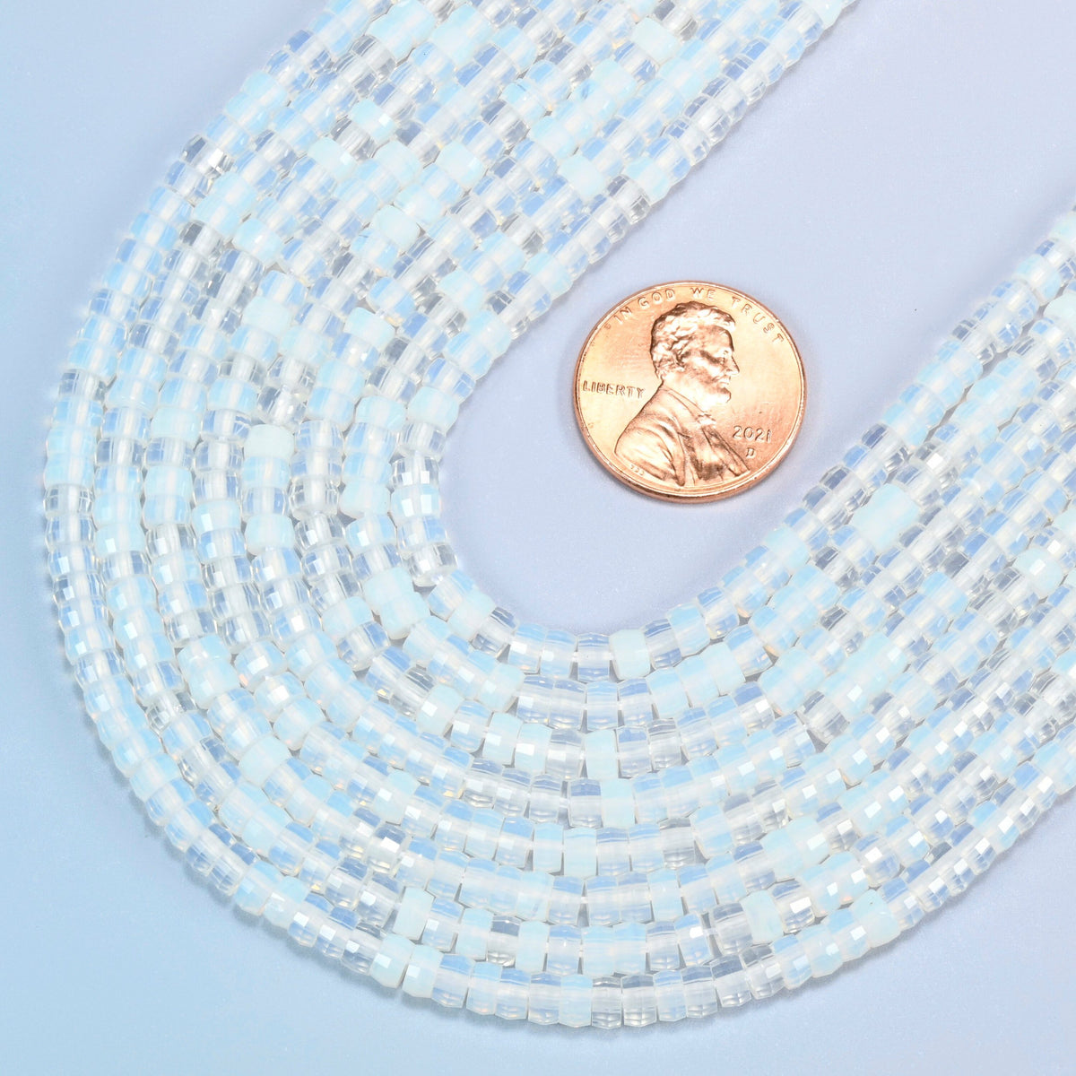 Close view of opalite faceted heishi disc strands curving beside a US penny for scale