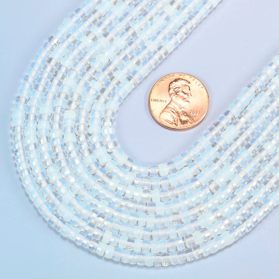Close view of opalite faceted heishi disc strands curving beside a US penny for scale