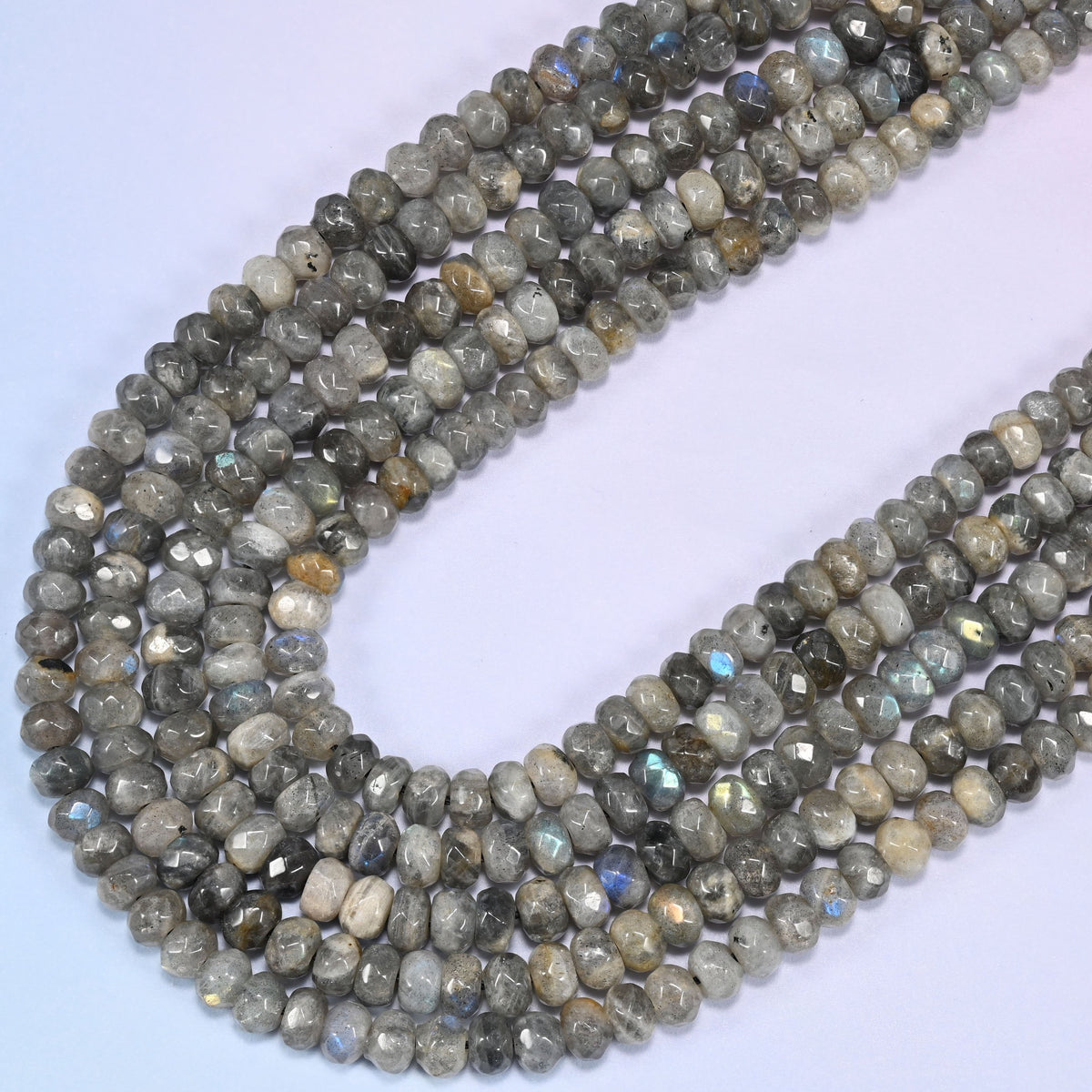 Gray Labradorite faceted rondelle beads curving in a long loop, cream and tan flecking scattered across the strand