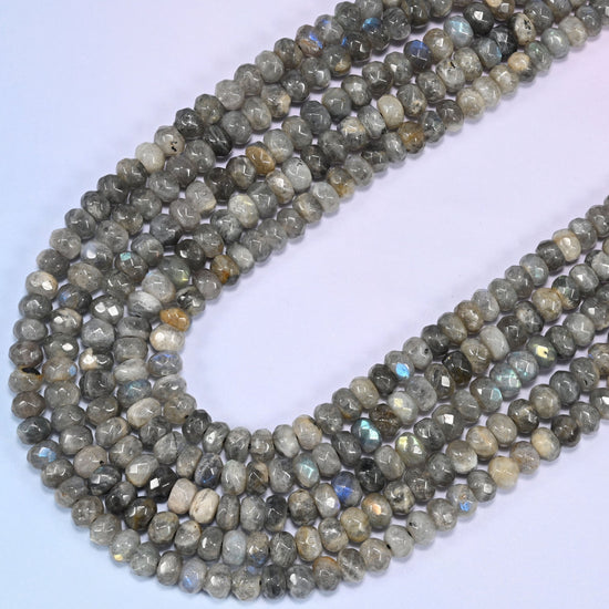 Gray Labradorite faceted rondelle beads curving in a long loop, cream and tan flecking scattered across the strand