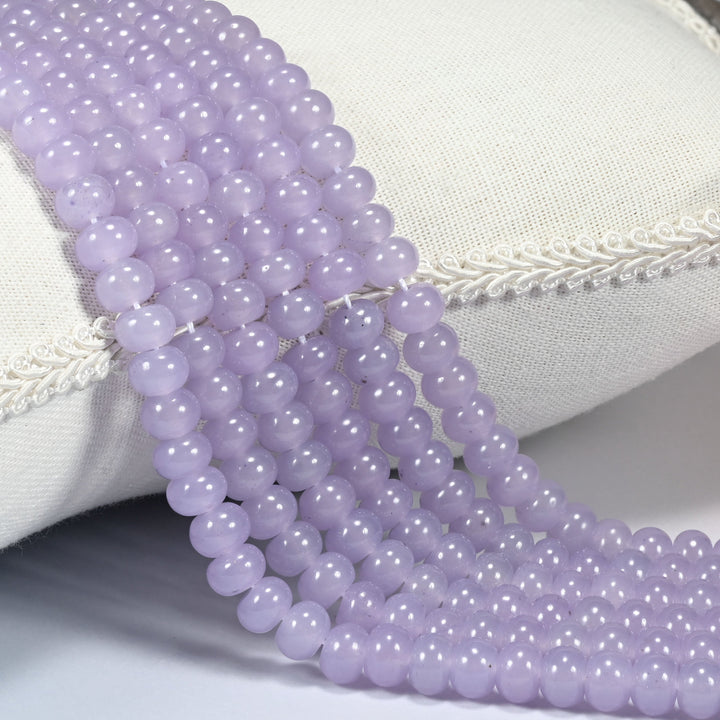 Taro Purple dyed jade gemstone rondelle beads draped over a cushion in soft rows, a soft muted taro purple, light and slightly dusty