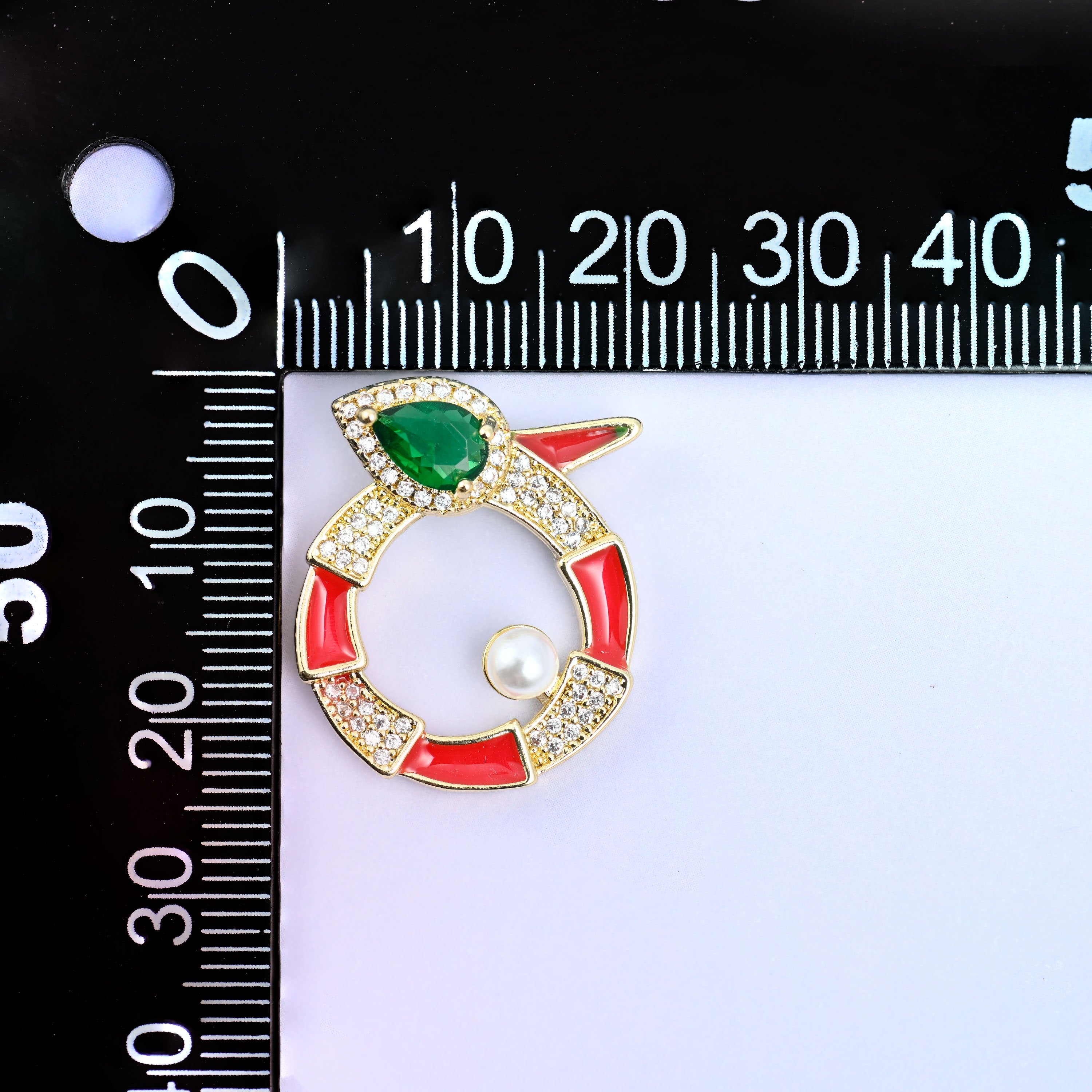 Round snake charm upright on a millimetre ruler, the red enamel ring and pearl set at the zero mark to show the width across the medallion.