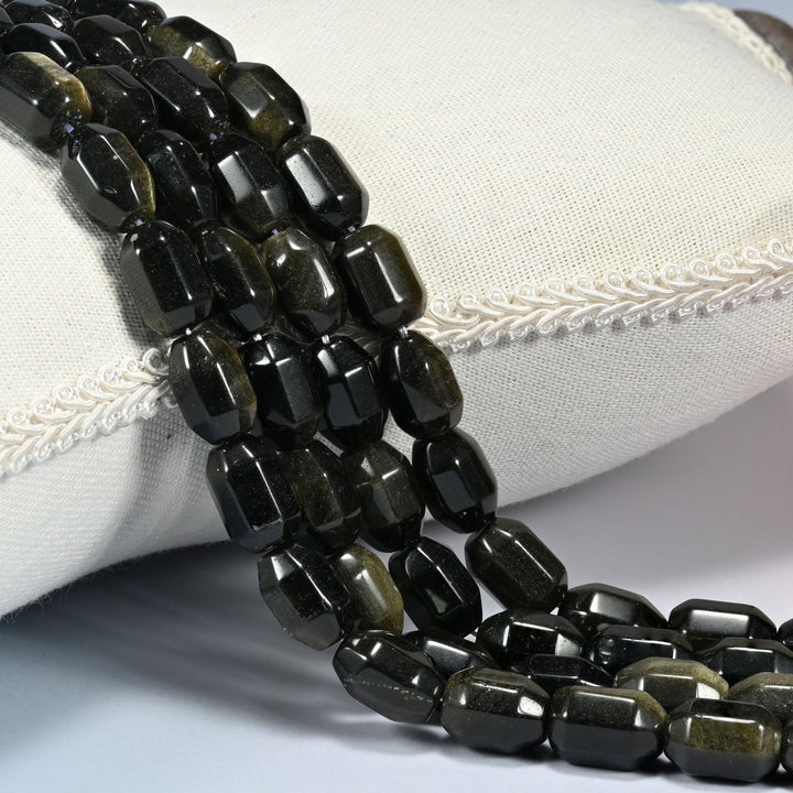 Gold Obsidian faceted barrel drum beads draped in a soft curve, a warm golden sheen sweeping across the near-black faces