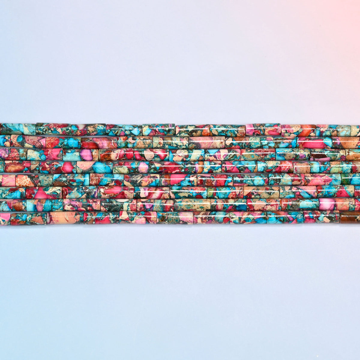 Several strands of dyed sea sediment jasper tube beads 13x4mm laid in straight rows, turquoise and pink tubes side by side