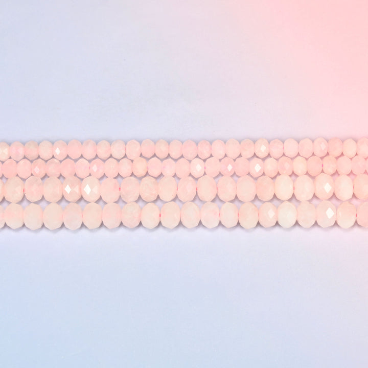 Rose quartz faceted rondelle beads laid in straight rows, showing the even rondelle shape and consistent bead size