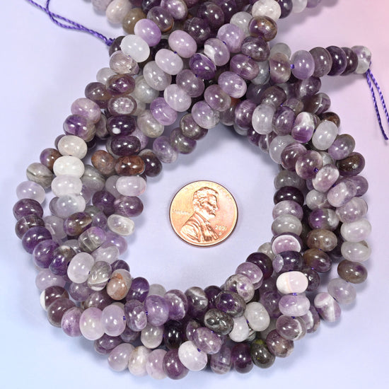 Multiple strands of Amethyst beads gathered together on a lavender surface, loose ends visible.