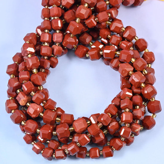 Deep brick-red opaque stone cut into faceted cubes, each flat face taking a glassy polish that flashes lighter terracotta as the strand moves.