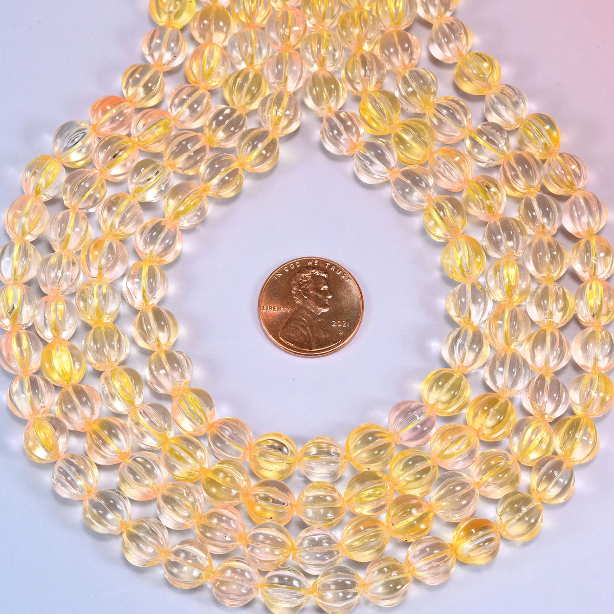 Yellow clear pumpkin glass beads, 8mm melon rounds, strands laid in a gentle wave straight across the frame.