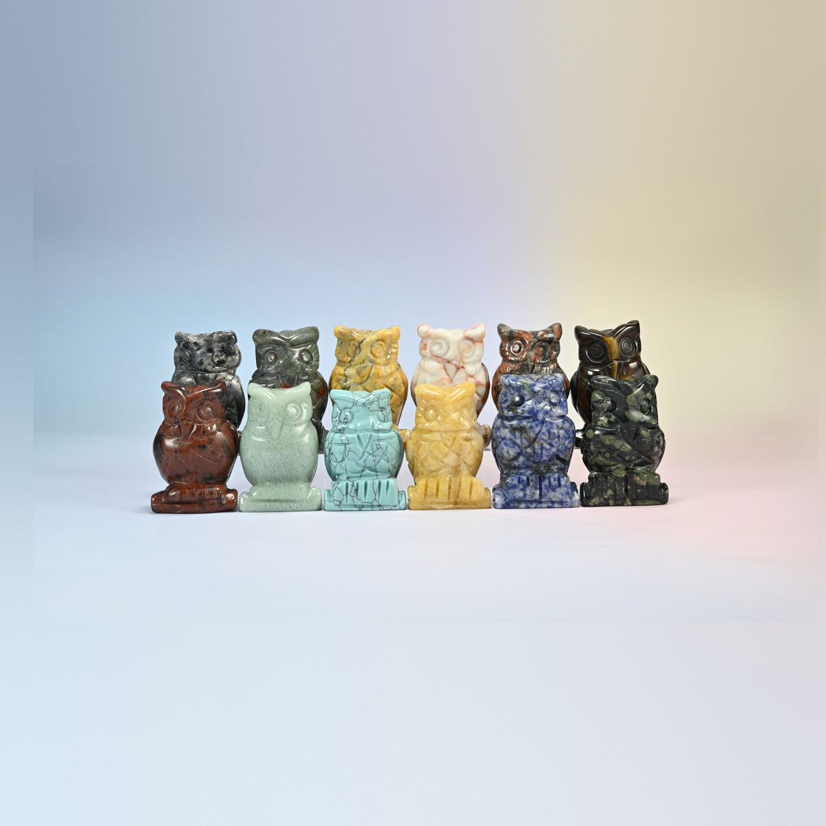 Row of owl crystal carvings in black labradorite, yellow jade, dyed green howlite, sodalite, tiger eye and more