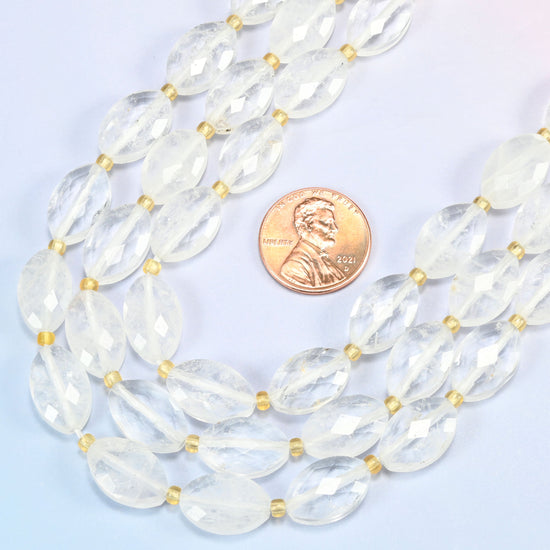 Close view of clear quartz faceted flat oval strands curving beside a US penny for scale