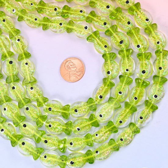 Iridescent Lime Green Fish Glass Beads — a small moulded fish in bright translucent lime, packed with fine glitter that catches the light from inside, with a clear tail and a single black eye dot.